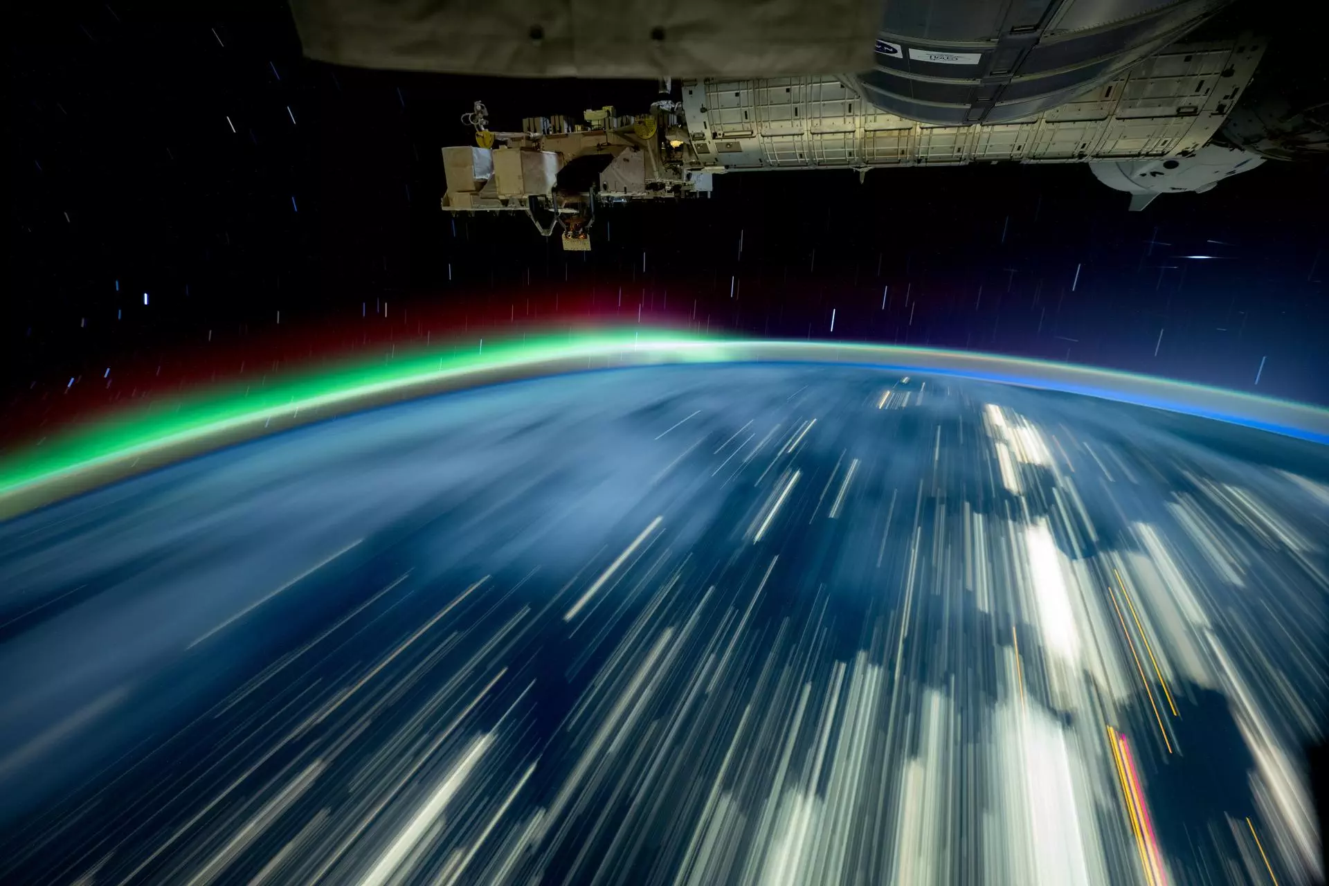 NASA Space Technology a long-exposure photo of earth with streaks of white and a green aurora on the horizon