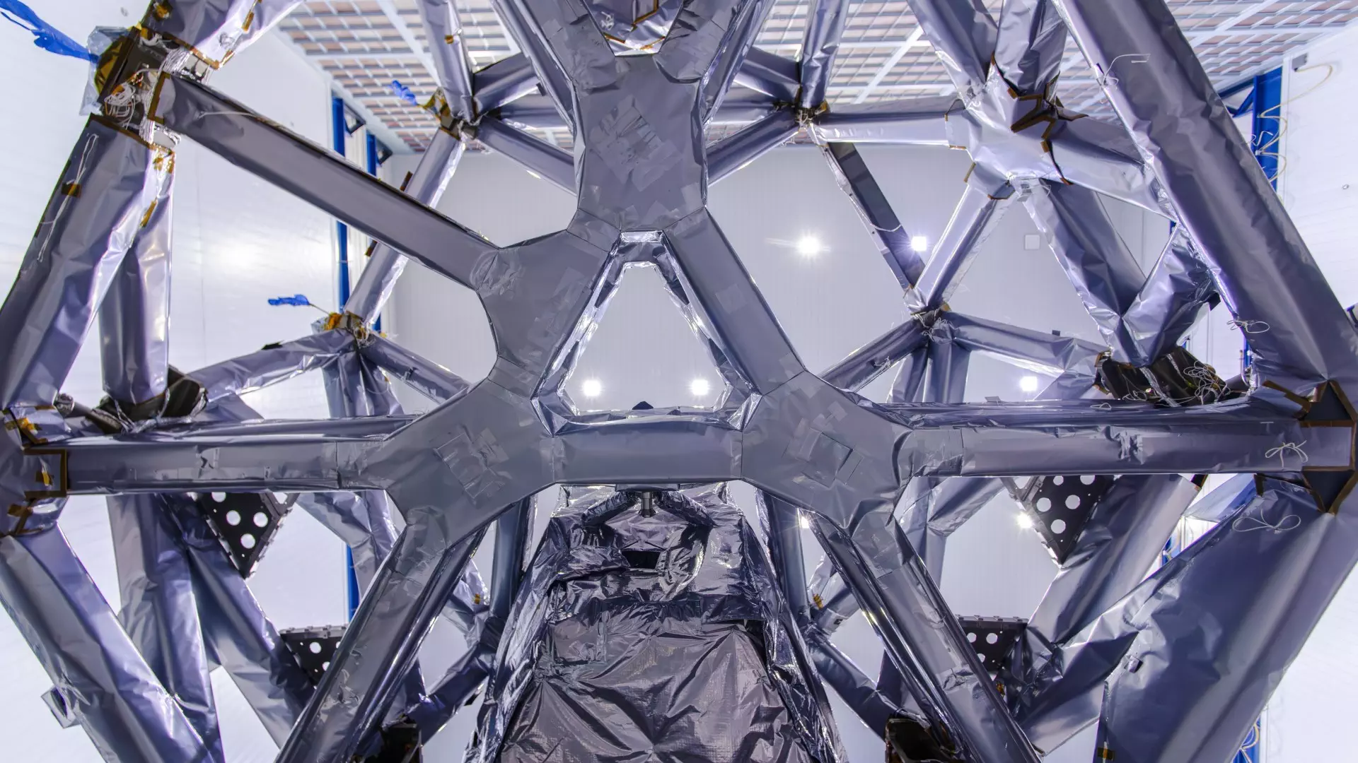 NASA Space Technology scientists in white clean suits move a metallic honeycomb-like structure onto a rectangular piece of electronics covered in wires and components