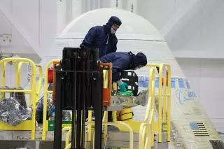 NASA Space Technology Two other folks are standing on a yellow-railed platform, inspecting gray, wrapped baggage.