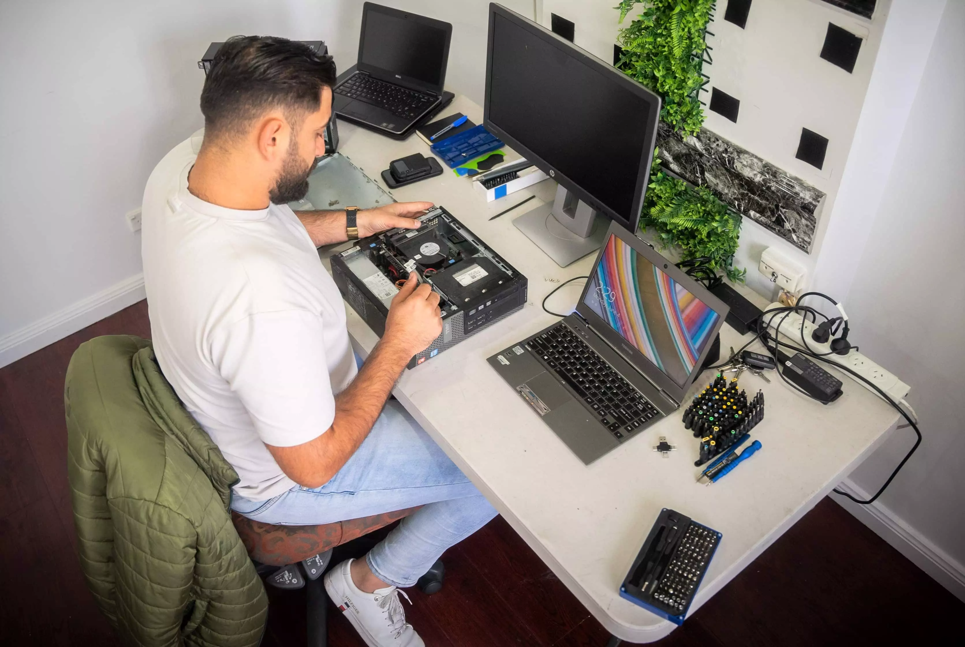 Technology tamfitronics A  man in a white t-shirt sits at a desk repairing a second hand pc.